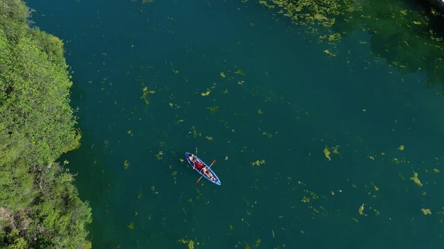 A couple in love canoeing and paddle boarding on a river with green water, algae, and water lilies; drone view of canoeing and kayaking in the Nera River gorges &ndash; Terni, Narni , Umbria, Italy