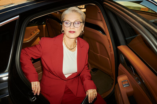 Caucasian senior businesswoman sitting in luxury car, preparing for arrival at corporate event, conveying executive success and premium lifestyle. Useful for leadership branding and luxury marketing