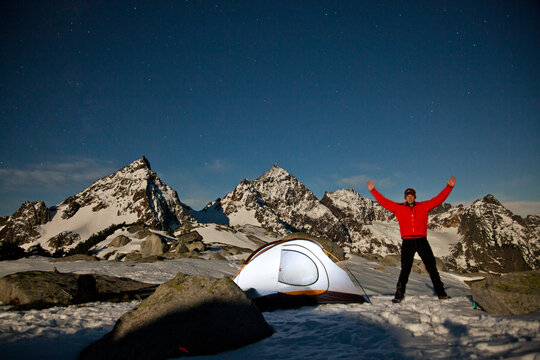 Joyful hiker camps in snowy mountains at night