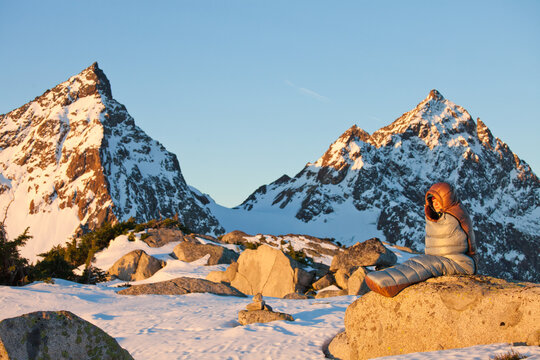 Woman in sleeping bag watches sunrise over mountains