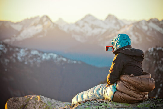 Hiker photographs a mountain sunrise from sleeping bag