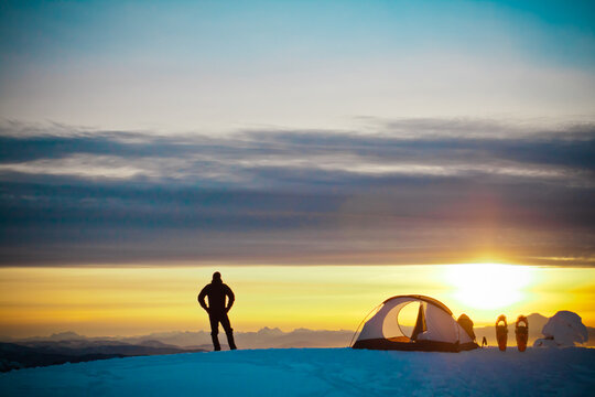 Solitary camper watching the sunset from a snowy summit