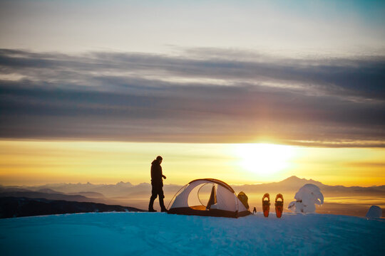 Solitary camper watching the sunset from a snowy summit