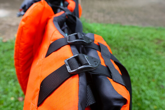 Bright orange life jacket with black straps and metal buckles resting on grass, outdoor safety equipment conveying preparedness and calm anticipation