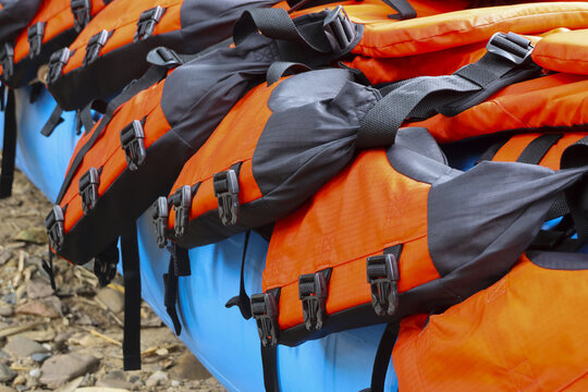 Bright orange life jacket arranged on blue kayak with black buckles and straps, outdoor gear ready for water adventure and safety on rocky shore