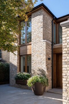 The entrance of a contemporary house features a stylish brick wall adorned with vibrant flower plants, all set against a backdrop of a clear blue sky on a beautiful sunny day