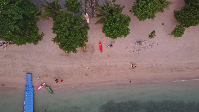 Panoramic aerial view of a calm tropical bay with sandy beach, long jetty pier, and dry hills under soft twilight sky in Labuan Bajo, Indonesia.