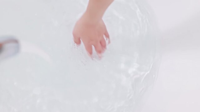 Young woman hands turning on faucet tap to run a bath of jacuzzi bathtub with foam soap and hand tests water temperature before enjoying self-care weekend day in hot water