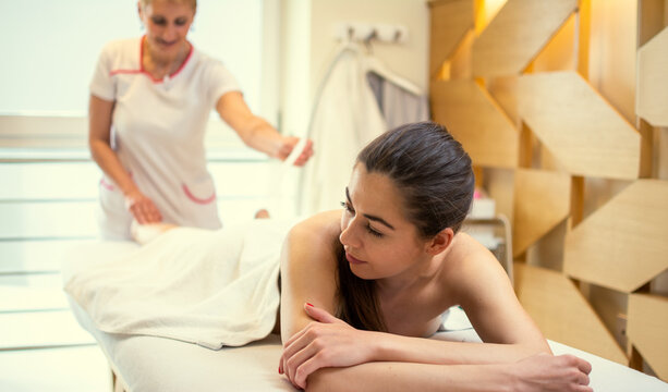 Beautician applying wax strip on woman leg during depilation procedure in salon