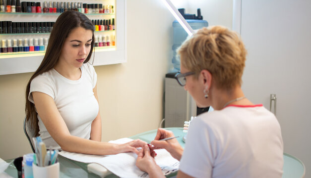 Professional manicurist using cuticle pusher during manicure procedure for client