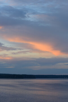 Beautiful vertical view of a tranquil sunset over a calm lake with vibrant pink and orange clouds in a deep blue evening sky.