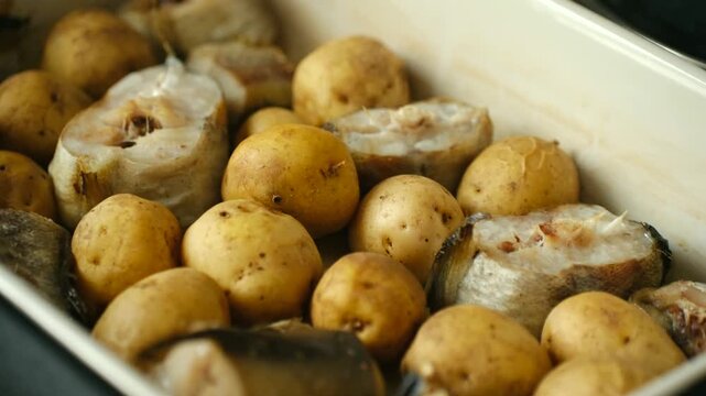 Hearty pollock fish pieces, whole young potatoes baking in ceramic dish, healthy nutritious homemade dinner, simple yet delicious traditional seafood recipe. Pollock fish with potatoes cooking in oven