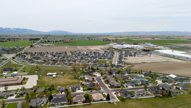 Aerial view of a residential subdivision next to industrial buildings and open fields.