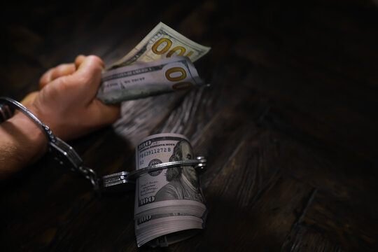 Hands of a fraudster with handcuffs on a background of us dollars. Fraud, cyber crime concept. Arrest of an entrepreneur in the workplace.