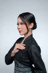 Profile portrait of an elegant Indonesian woman touching her chest in a black lace kebaya. © Saddha Visual