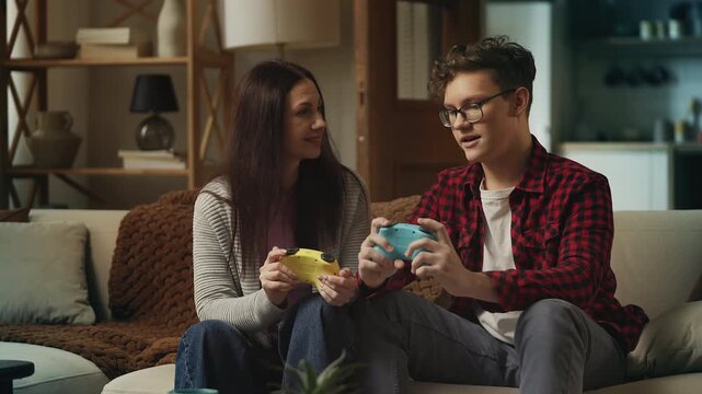 Happy teen boy teaching his mom to play a video game using a game controller