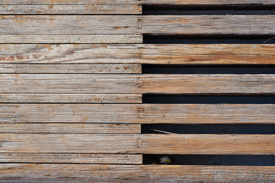 A top view of old weathered grey and brown wooden boardwalk planks showing natural grain textures and parallel linear gaps under sunlight
