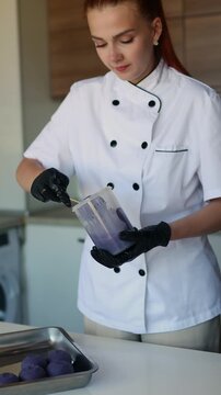 Female pastry chef glazing cake pop with purple chocolate coating