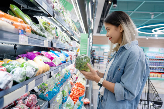 Young asian woman choosing vegetables while shopping food in supermarket