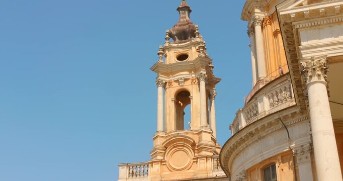 Close view of the Basilica of Superga bell tower and facade in Turin, Italy, framed against a clear blue summer sky.