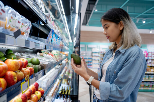 Choosing the best vegetables. A side view of a smiling Asian woman selecting fresh fruits and vegetables at a supermarket.