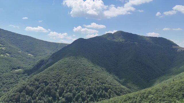Montagne ricoperte di vegetazione verde con pendii morbidi, giochi di luce e ombra e cielo azzurro con nuvole bianche sparse
