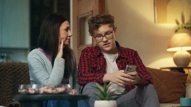 Teen boy teaching his mother to use a new social media app on her cellphone