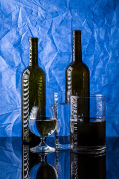 Still life with bottles and glasses with liquid on blue background
