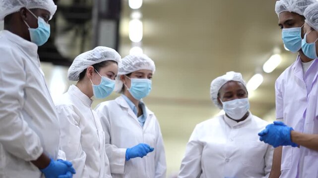 Food factory workers standing in circle and discussing production before shift. Teamwork, communication, production planning, food manufacturing, factory operations, workplace collaboration.