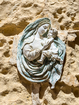 A bas‑relief plaque of the Virgin Mary and Child mounted on a limestone wall in Mdina, Malta, featuring delicate carved details, classical drapery and warm Mediterranean light on the stone surface