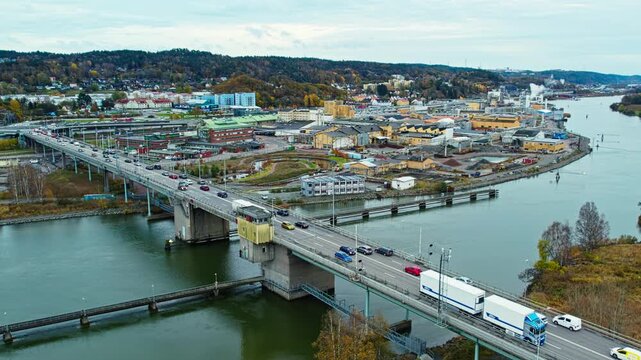 Aerial drone view of the Jordfallsbron bridge crossing the G&ouml;ta &auml;lv river in Sweden. Heavy traffic moves along the highway while industrial buildings line the riverbank under an autumn sky.