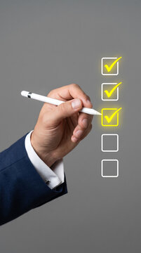 Hand holding a stylus pen checking off a todo list with check marks on a gray background in a professional setting for productivity