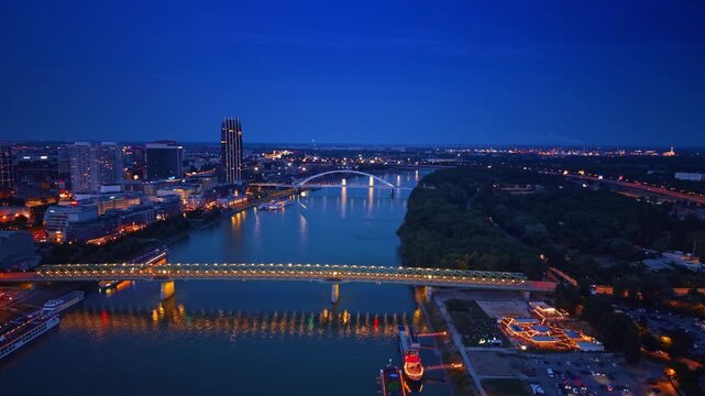 Night aerial skyline of Bratislava with bridges over Danube river. Illuminated Old Bridge and Apollo Bridge crossing water near tall modern buildings.