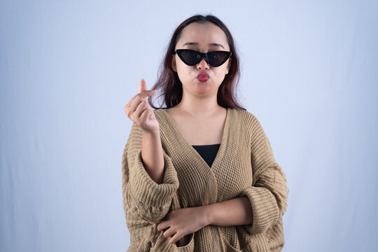 Young Asian woman in sunglasses making finger heart gesture against white background