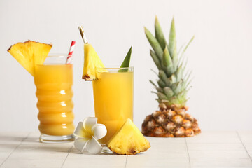Obraz premium Glasses of fresh pineapple juice with flower on tile table near white wall