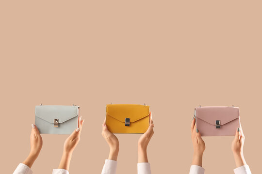 Female hands with different stylish womens bags on beige background