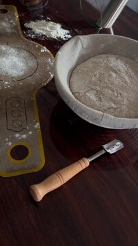 Artisan sourdough baking set with dough in proofing basket and tools on wooden table