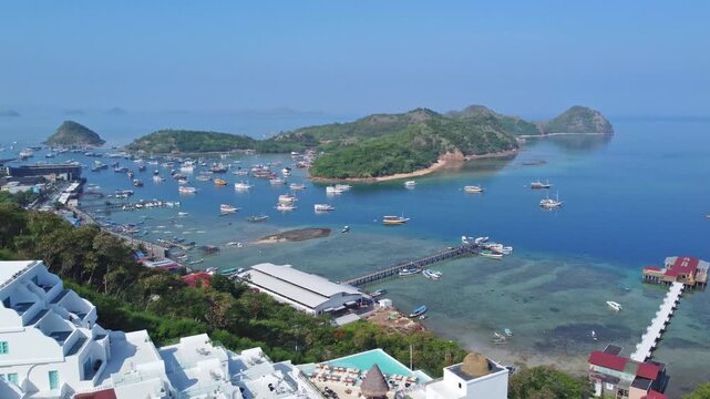 Shutterstock Title / Description
Panoramic aerial view of Labuan Bajo bay filled with anchored boats, wooden jetties, white hillside resort villas, and tropical islands in Indonesia.