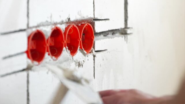 Fixing orange plastic socket box into wall with plaster putty