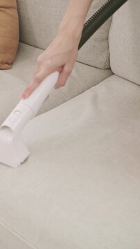 Close up shot of a person using a vacuum cleaner to clean a white fabric sofa in the living room.
