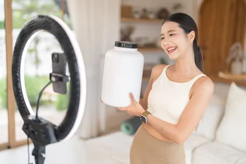 Fitness asian influencer creating social media content with smartphone and ring light, Content creator live streaming health supplement product mockup at home, Vlogger, active lifestyle and wellness © Art_Photo