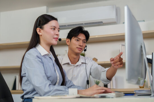 Asian coworkers with headsets collaborating and pointing at computer screen in office
