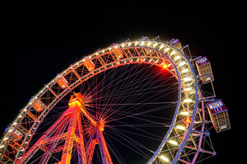 A brightly illuminated Ferris wheel photographed from a dramatic low angle against a black night sky. Ideal for travel, entertainment, tourism, festivals, and urban nightlife themes. © Duro Mesiar