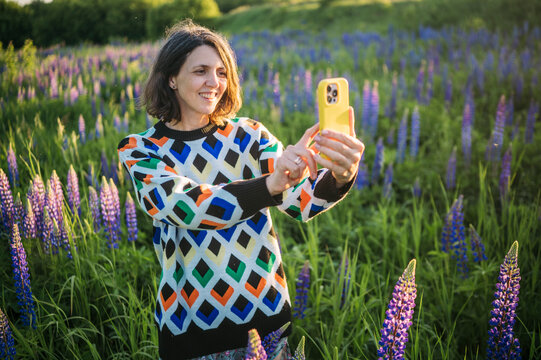 Woman shoots a selfie outside in a field of purple lupines