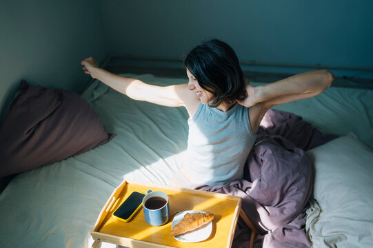 Person stretching in bed with a morning breakfast tray