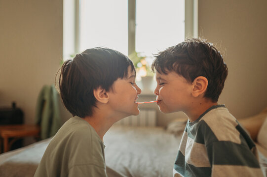 Brothers share a long candy while playing in the bedroom