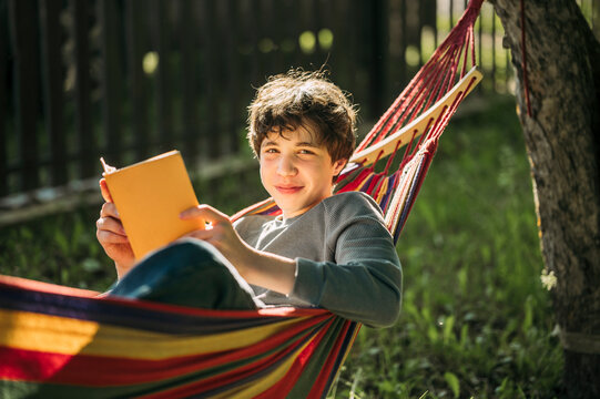 Smiling boy reads a book while relaxing in a hammock outdoors