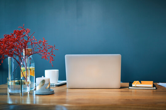 Laptop with diaries and decorations on desk against blue wall in home office