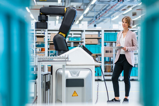 Businesswoman with tablet in a modern factory hall looking at robot