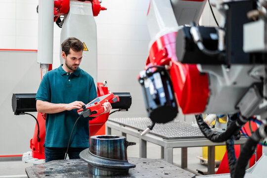 Male engineer operating robotics through control while standing in factory